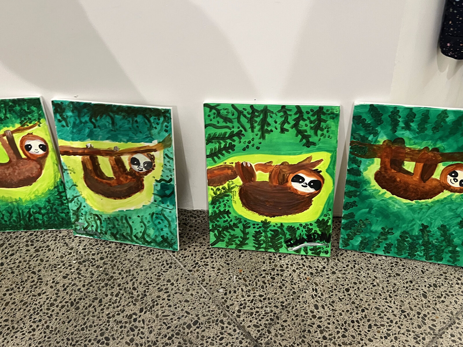 Four paintings of sloths hanging from branches in green jungles, lined up in a row